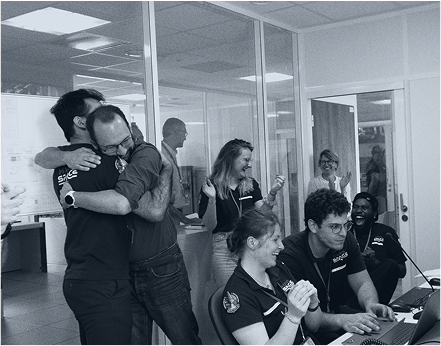 Spontaneous moment of joy among HyPrSpace engineers during a successful test, showing team members smiling and cheering in a brightly lit control room.